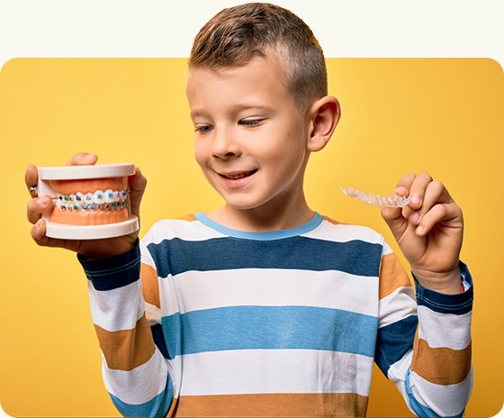 young boy holding braces and invisalign